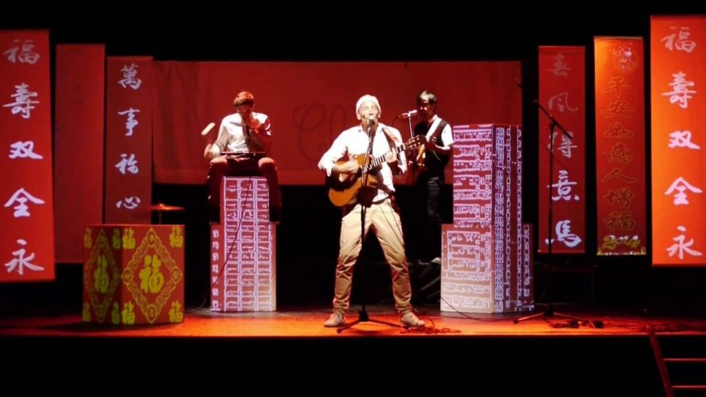 Merlot chante et joue de la guitare sur scène aux côtés de Svent, entourés de bannières chinoises